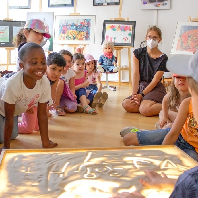 Eine Gruppe von Kindern mit zwei Aufsichtspersonen, umgeben von einer Galerie mit vielen Bildern. (vergrößerte Bildansicht wird geöffnet)