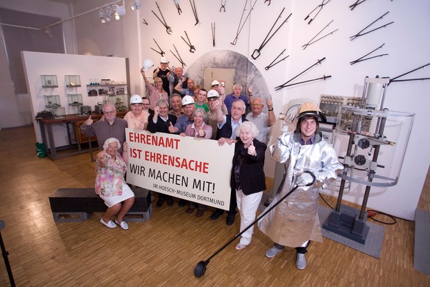 Ehrenamtliche im Hoesch-Museum Dortmund, die ein Plakat mit der Aufschrift: "Ehrenamt ist Ehrensache - Wir machen mit!" hochhalten