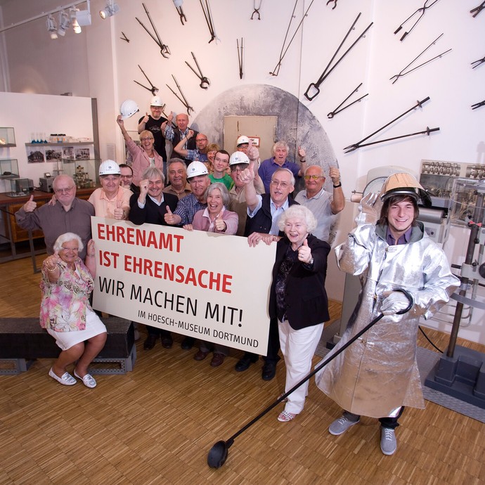 Ehrenamtliche im Hoesch-Museum Dortmund, die ein Plakat mit der Aufschrift: "Ehrenamt ist Ehrensache - Wir machen mit!" hochhalten (vergrößerte Bildansicht wird geöffnet)