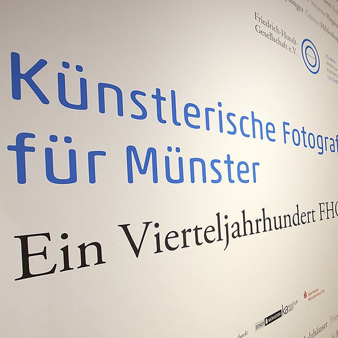 Ausstellungswand mit der Aufschrift: "Künstlerische Fotografie für Münster - Ein Vierteljahrhundert FHG" (vergrößerte Bildansicht wird geöffnet)