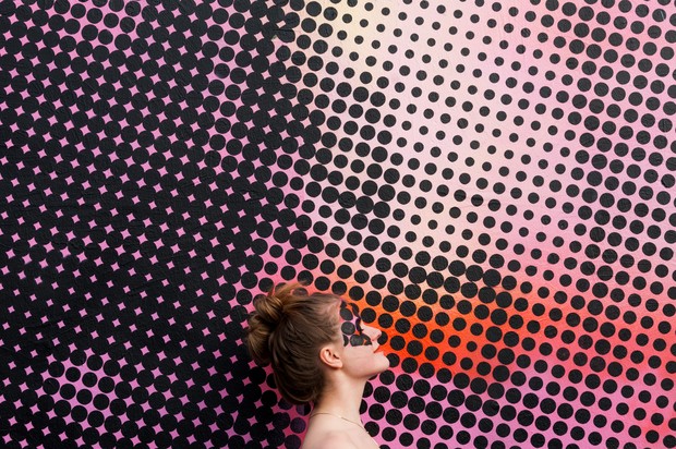 Frau vor einem abstrakten Hintergrund mit schwarzen Punkten und rosa-rot-pinker Farbe