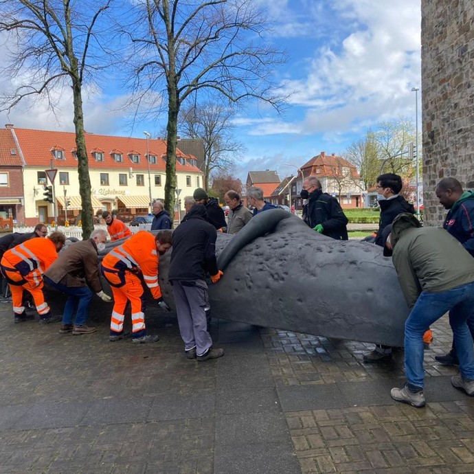 Anlieferung der Walskulptur - Ehrenamtliche und Hauptamtliche tragen den Wal gemeinsam in das Ausstellungsgebäude (vergrößerte Bildansicht wird geöffnet)