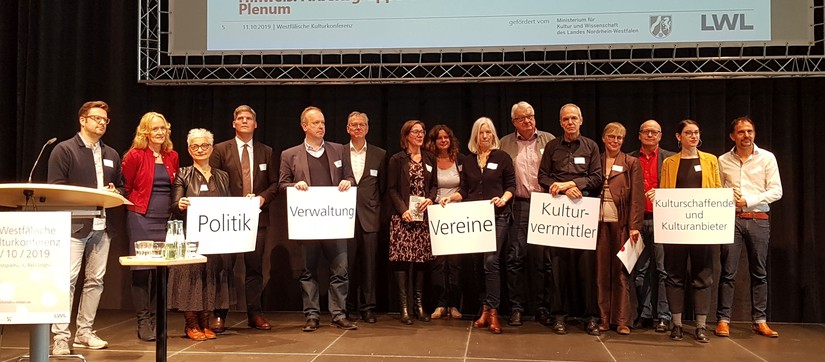 Konferenzteilnehmende auf der Bühne mit Schildern in der Hand