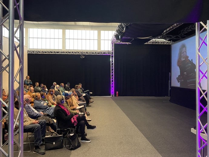 Konferenzteilnehmer:innen in der Video-Lounge des Info-Parcours (vergrößerte Bildansicht wird geöffnet)